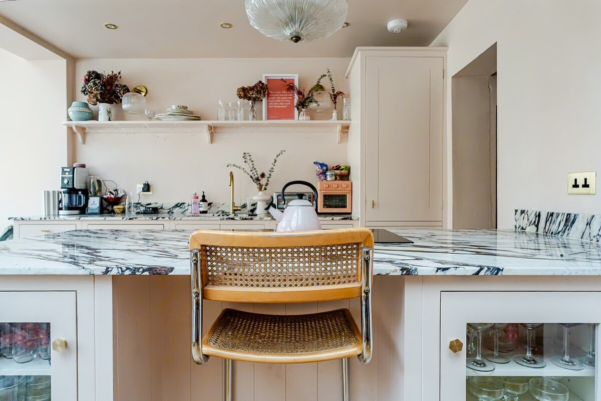 Pink shaker kitchen with marble worktop, cane bar stool and pastel kettle